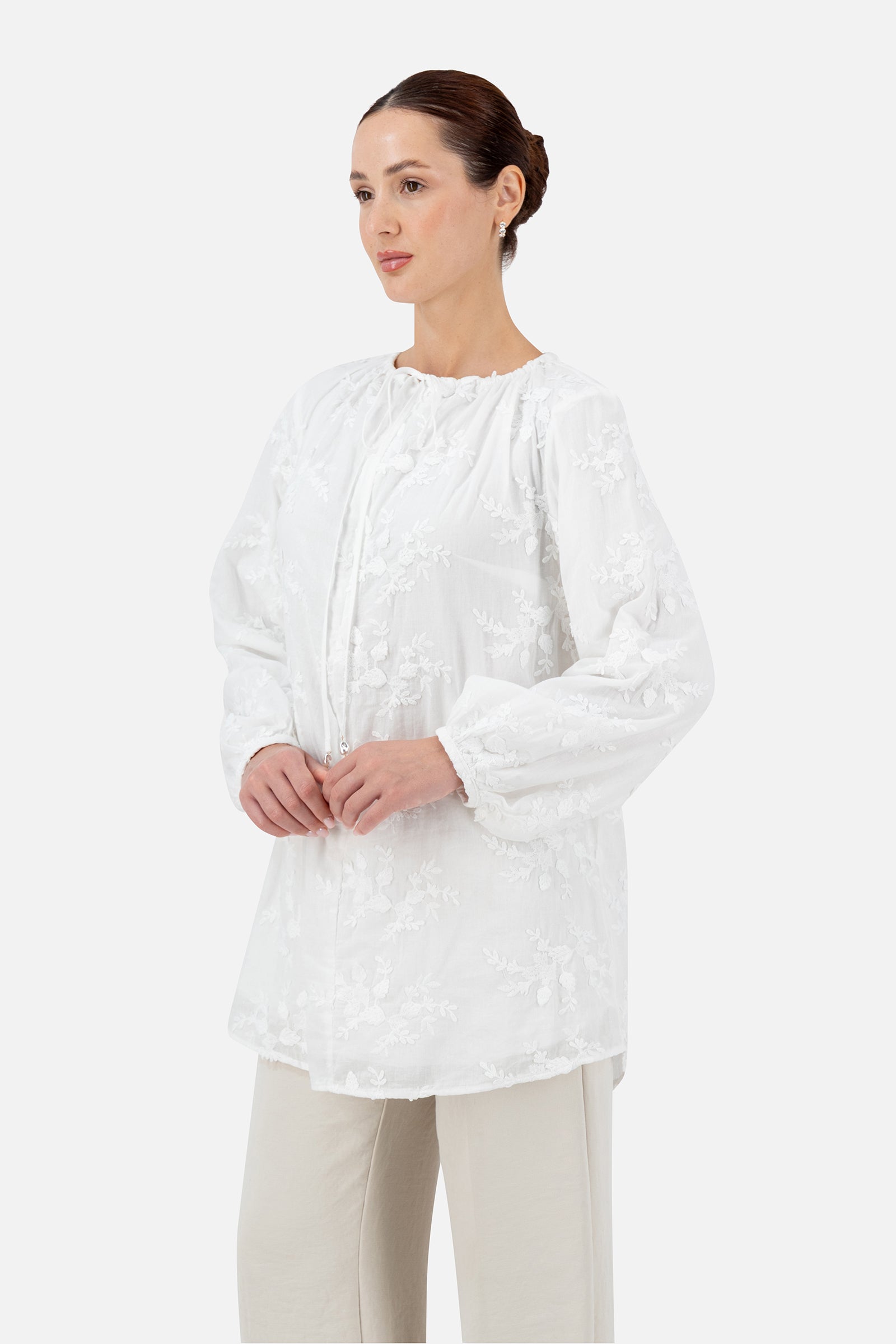 Woman standing in a white floral embroidered blouse and matching pants.