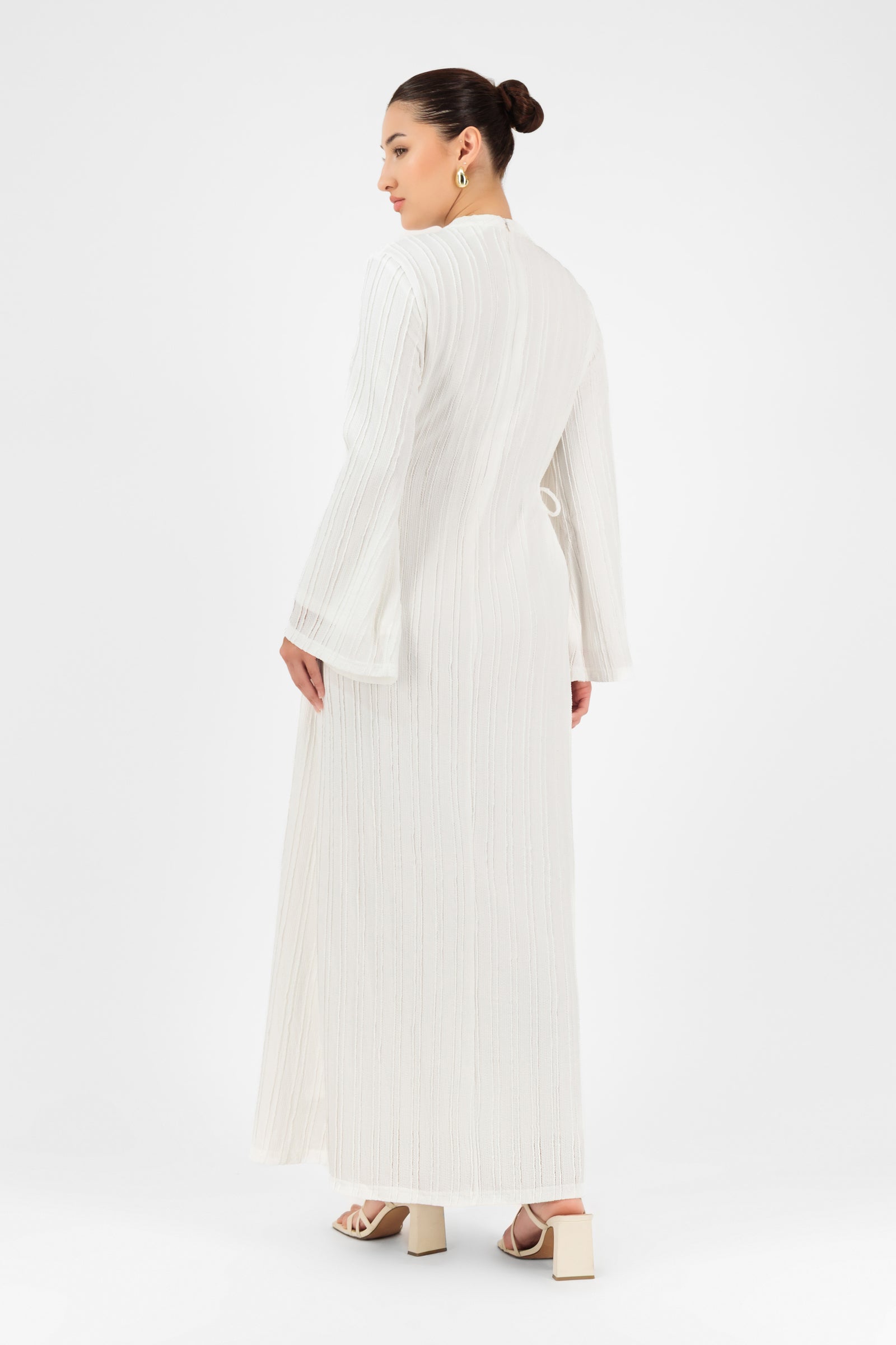 Woman turning slightly in the white FARES maxi dress showcasing the elegant drape and wide sleeves from the back.