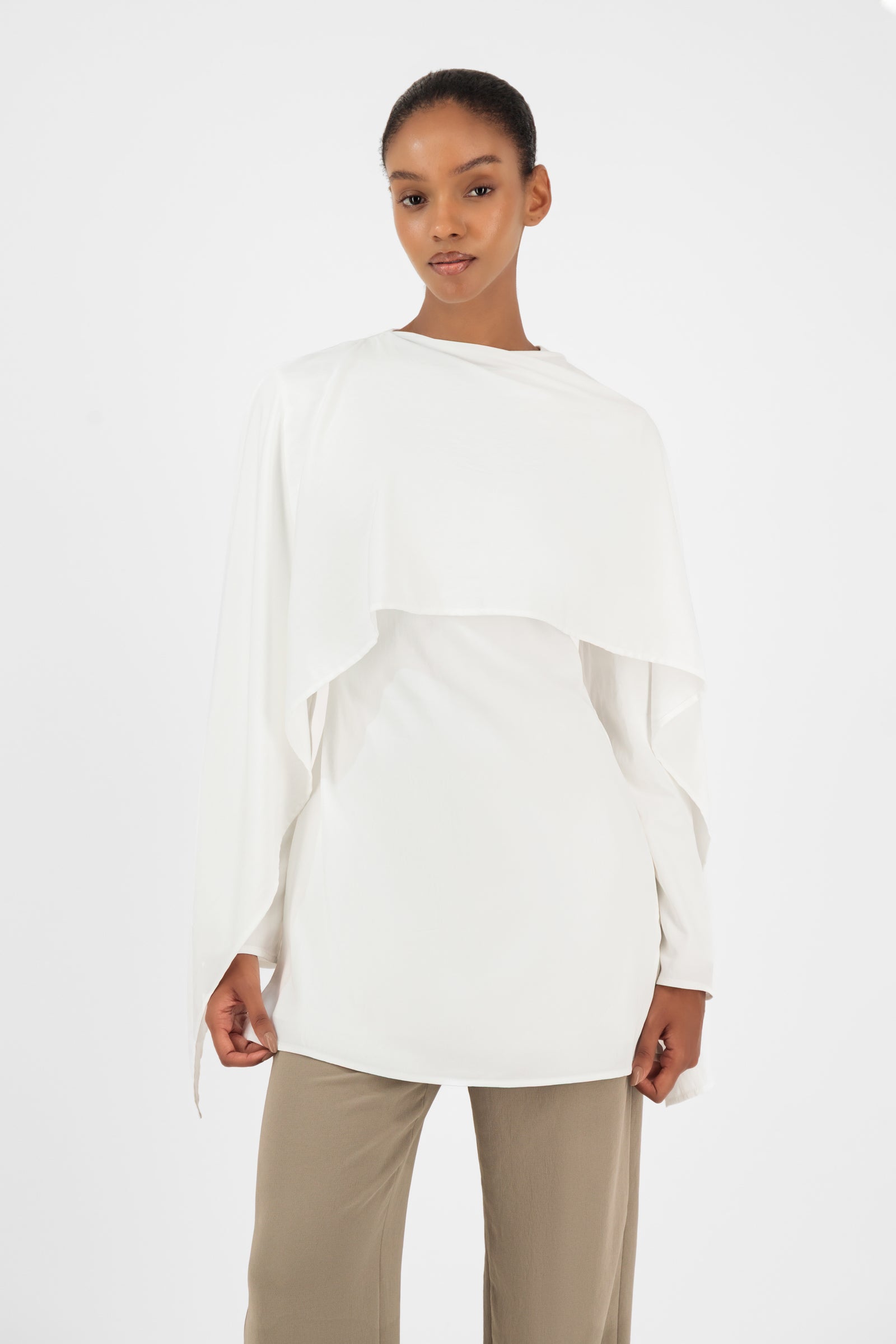 Model standing in the FARES Cape Overlay Tunic in White featuring a flowing tunic silhouette with elegant layered detailing.