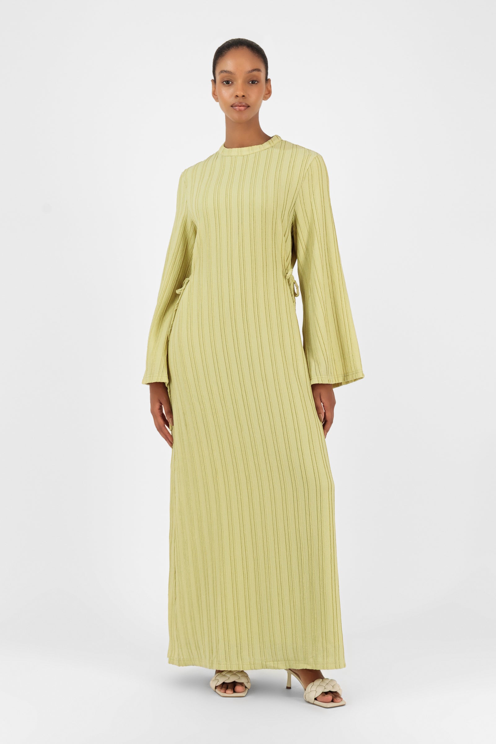 Model standing in the FARES Textured Bow Detail Dress in Lime featuring a flowing maxi dress silhouette with soft textured detailing.