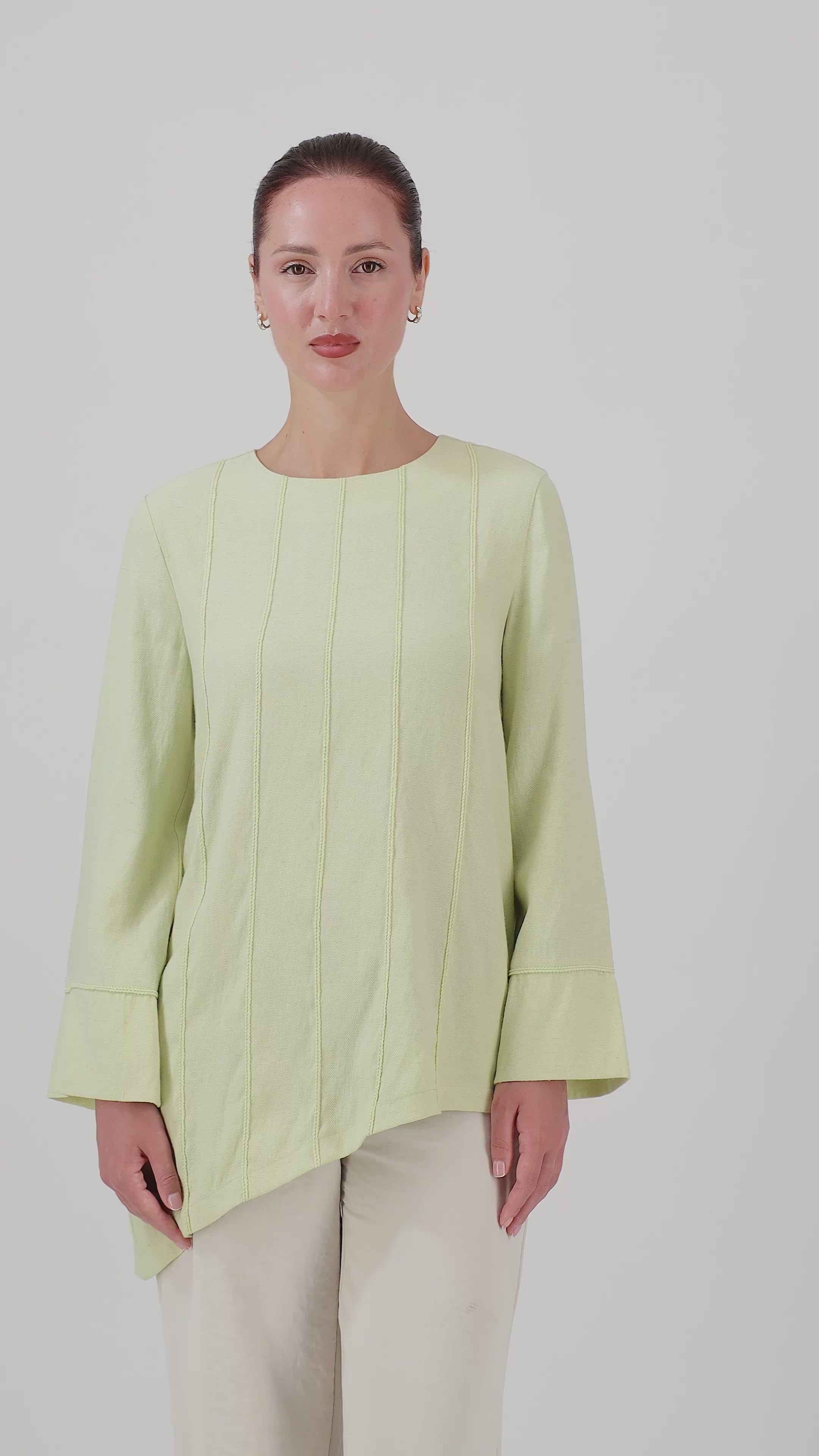 A woman walks in the FARES Braid Detail Slanted Tunic in Honeydew, showcasing the flowing asymmetric silhouette and natural movement of this tunic.