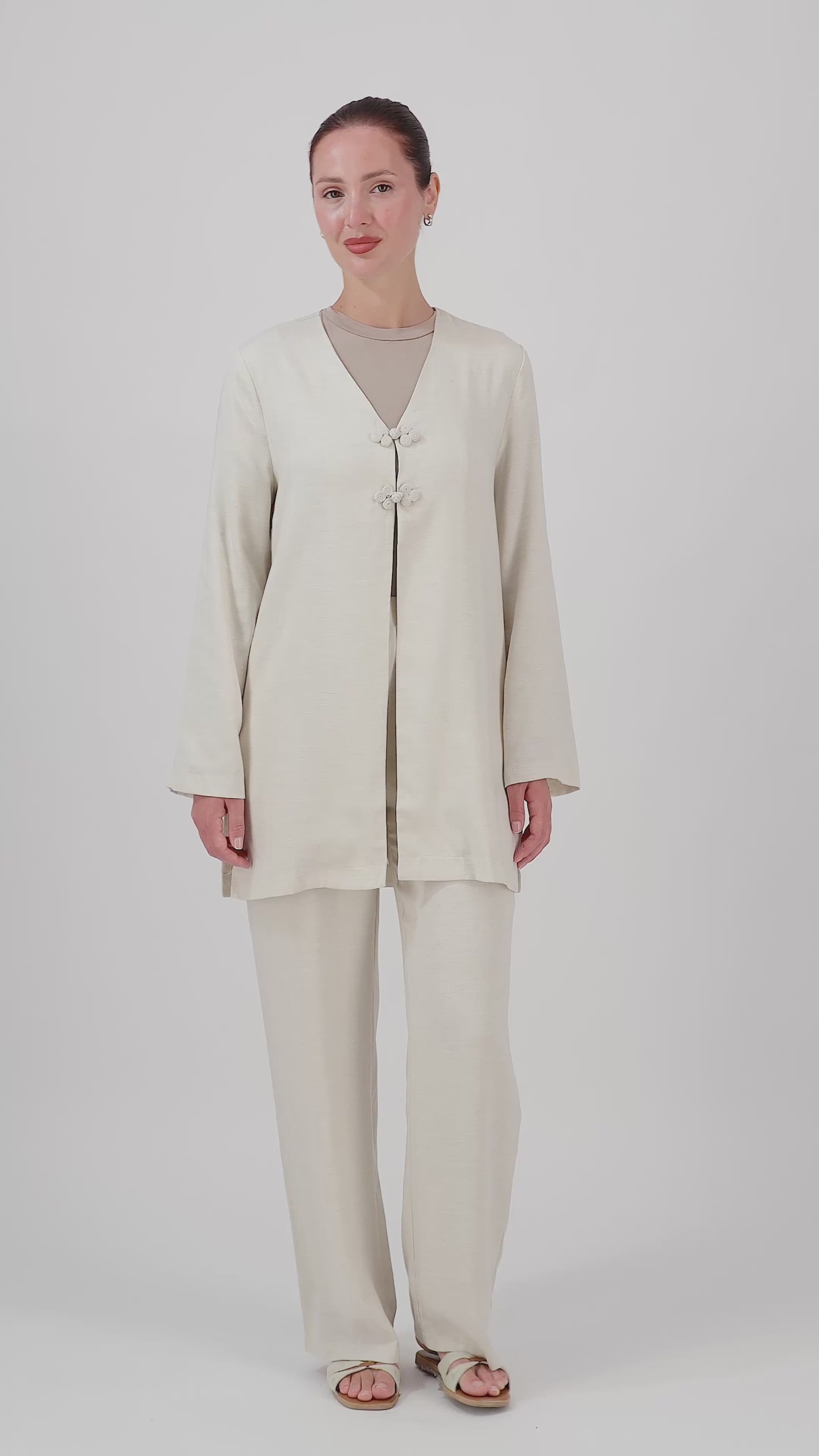 A woman walks in the FARES Knot Detail Cardigan in Bare, showcasing the flowing sleeves and natural movement of this wide-sleeve cardigan.