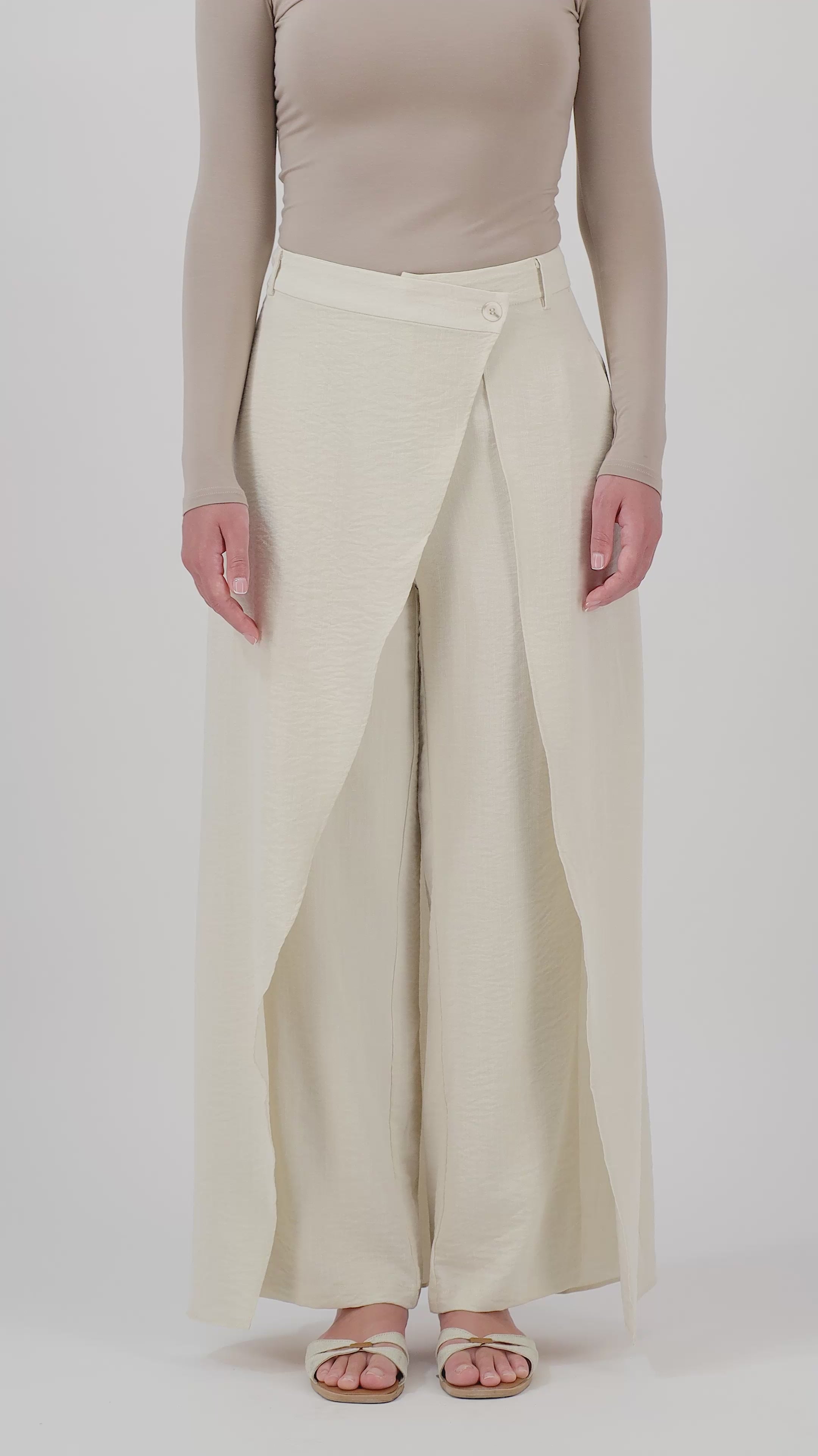 A woman walks in the FARES Skirt Overlay Trousers in Oats, showcasing the movement of the skirt overlay and flowing wide-leg trousers.