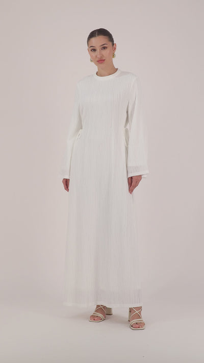 A model walking in the FARES Textured Bow Detail Dress in White showcasing the fluid silhouette of the maxi dress.